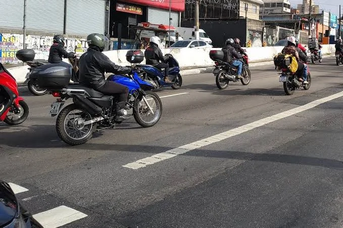 Motociclistas de capacete numa avenida brasileira
